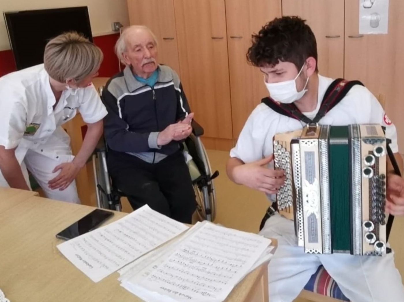 Ein Zivildiener spielt im Seniorenkompetenzzentrum Ahornhof das Akkordeon, eine Seniorenbetreuerin und ein älterer Herr hören zu